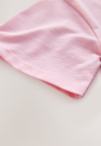 Rosa bomullstyg med en mjuk textur, med en enkel design och en prydligt sydd fåll vid ärmkanten.