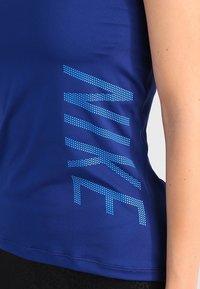 Canotta atletica blu con logo Nike testurizzato in pois blu, design aderente e tessuto morbido. Ideale per l'abbigliamento sportivo.