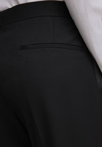 Schwarze Hose mit glatter Stoffstruktur, schmaler Passform und einem klaren Design mit einer unauffälligen Hintertasche.