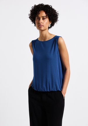 Haut sans manches bleu avec un col arrondi, en tissu doux, détails froncés aux épaules et coupe relaxée, associé à un pantalon noir.