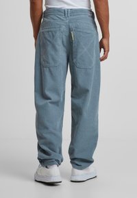 Pantalones de pana azul claro con un ajuste relajado, detalles de costura visibles, dos bolsillos traseros y zapatillas blancas.