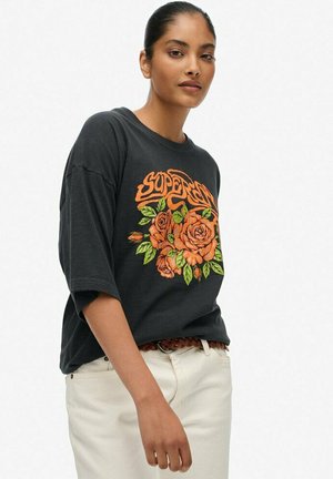 T-shirt noir surdimensionné avec un graphisme floral orange comprenant des roses et le mot "SUPERDRY". Matière en coton doux avec des manches courtes.