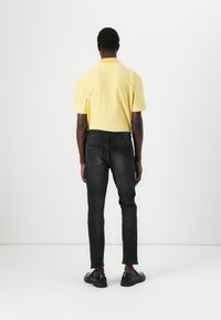 Cămașă polo galbenă cu mânecă scurtă, blugi negri slim-fit, pantofi negri. Design simplu cu guler și detalii de cusătură pe cămașă.