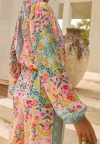 Floral-print, light fabric outfit featuring long sleeves, gathered waist, and pastel colors with detailed patterns of flowers and foliage.