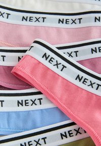 Sous-vêtements empilés de couleurs pastel avec des bandes élastiques blanches à la taille portant le nom de la marque « NEXT » en lettres noires.