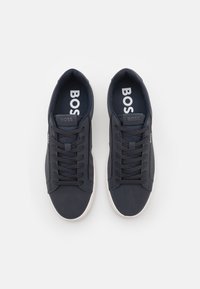Baskets bleu marine avec une texture lisse, dotées d'une semelle en caoutchouc blanche, d'un design à lacets et d'un logo 'BOSS' visible sur la languette.