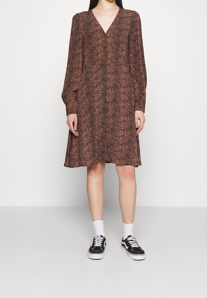 Abito a fantasia leopardata marrone con maniche lunghe, scollatura a V, silhouette fluida e orlo all'altezza del ginocchio, abbinato a sneaker nere e calzini bianchi.