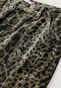 Leopardmønstret denimstof med forskellige sorte pletter på en grønbrun baggrund, med en topknap, små sølvdetaljer og stikninger.
