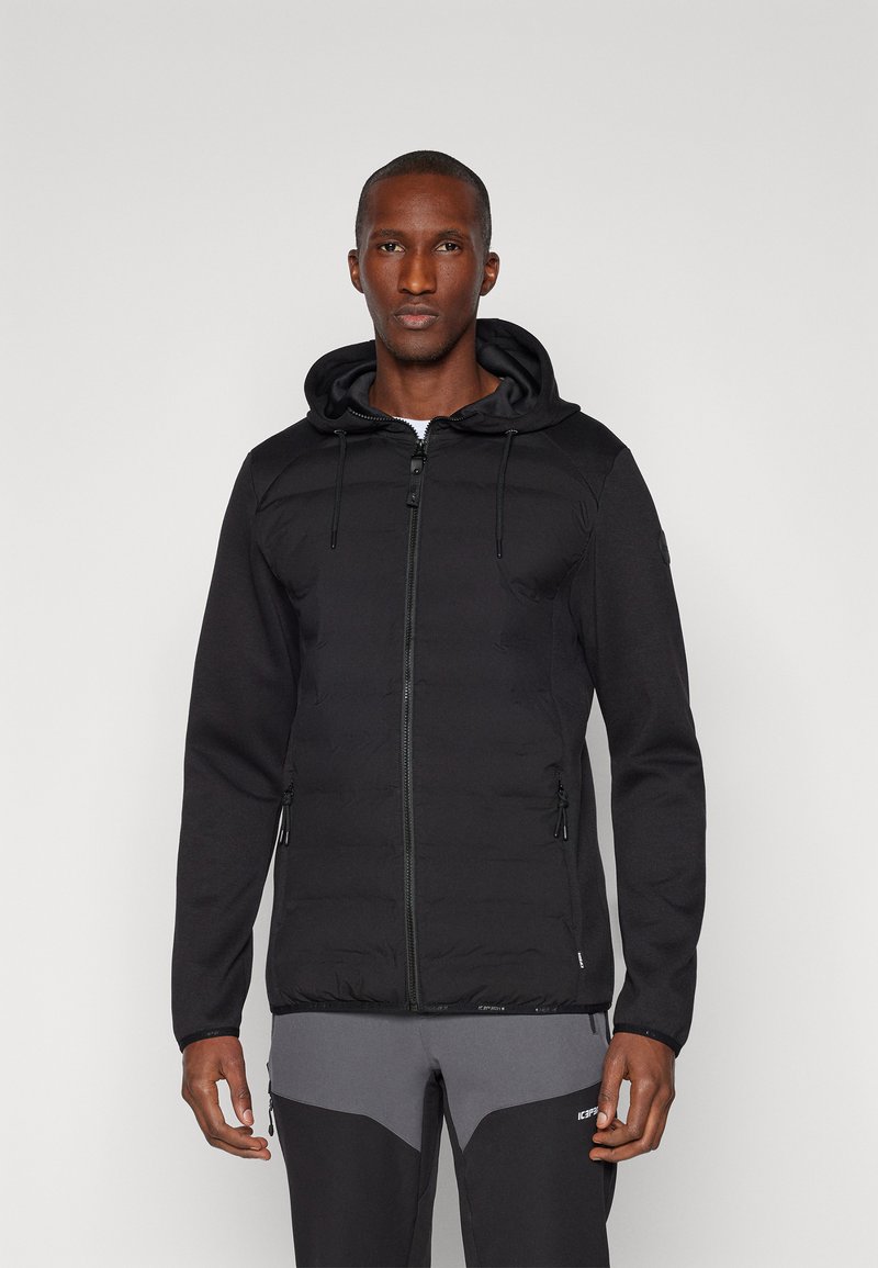 Giacca ibrida nera con zip frontale, torso imbottito e maniche in fleece. Presenta un cappuccio, tasche con zip e un design aderente.