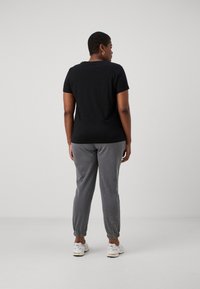 Black short-sleeve t-shirt paired with gray sweatpants, featuring elastic cuffs, with a smooth texture. White sneakers with subtle design.