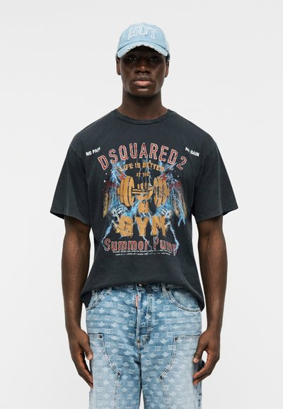 Άνδρας που φοράει μαύρο γραφικό μπλουζάκι "Dsquared2 Gym Summer Pump", ανοιχτόχρωμο μπλε τζιν με σχέδια και ανοιχτόχρωμο μπλε καπέλο με το κείμενο "HOT".