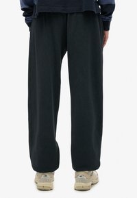 Pantalones amplios negros hechos de tela suave, con un ajuste relajado y detalles de costura sutiles, combinados con zapatillas deportivas beige.