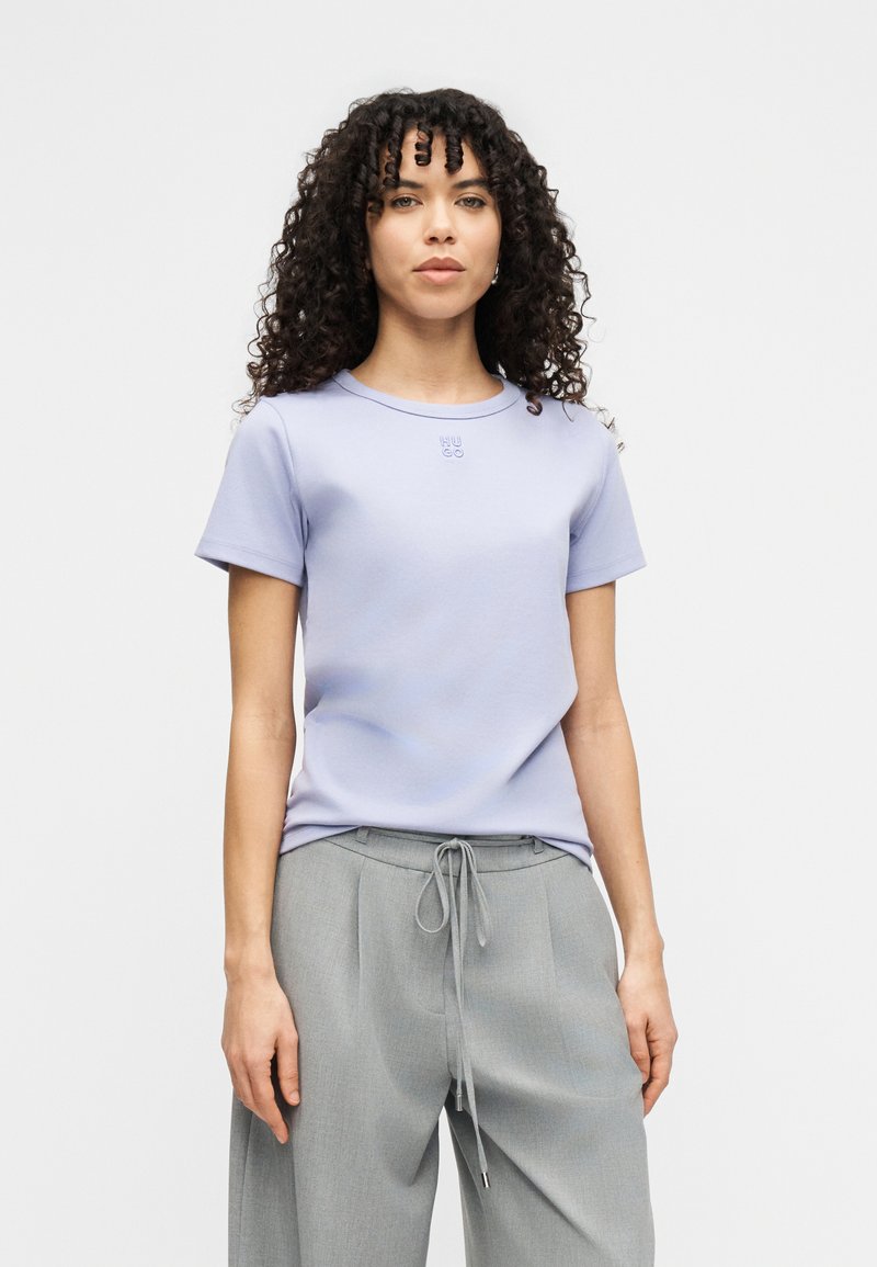 Ανοιχτό μωβ κοντομάνικο T-shirt με στρογγυλή λαιμόκοψη και κεντημένο λογότυπο. Συνδυασμένο με γκρι παντελόνια με κορδόνι για άνετη εφαρμογή.
