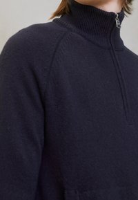 Marinblå stickad tröja med hög krage och halv dragkedja. Ribbad struktur och sömlös design. Har en minimalistisk stil och en avslappnad passform.