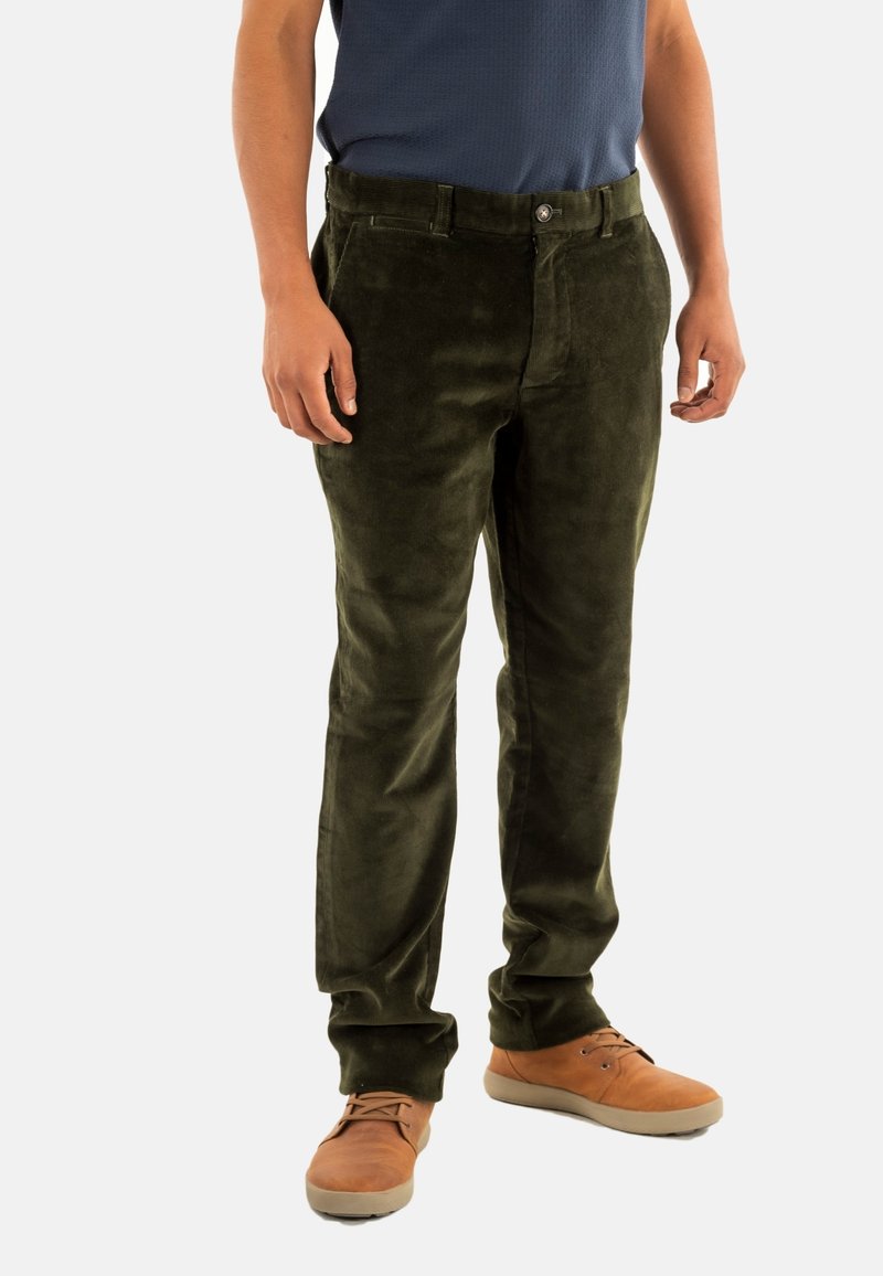 Pantalons en velours côtelé vert olive avec une texture lisse, coupe droite, fermeture à bouton et passants de ceinture. Portés avec des chaussures marron clair.