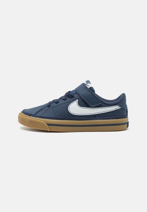 Marineblå sneaker med hvid Nike-swoosh, velcrobånd, sorte snørebånd og sål af gummigummi, vist i venstre sideprofil på hvid baggrund.