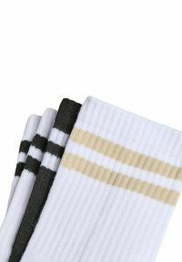 Trzy pary skarpetek: jedne białe z beżowymi paskami, jedne białe z czarnymi paskami oraz jedne całkowicie czarne, wszystkie o prążkowanej fakturze.