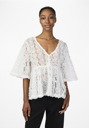 Blouse blanche avec un design texturé floral composé de roses en tissu superposées, avec un col en V, des manches courtes et une coupe ample.