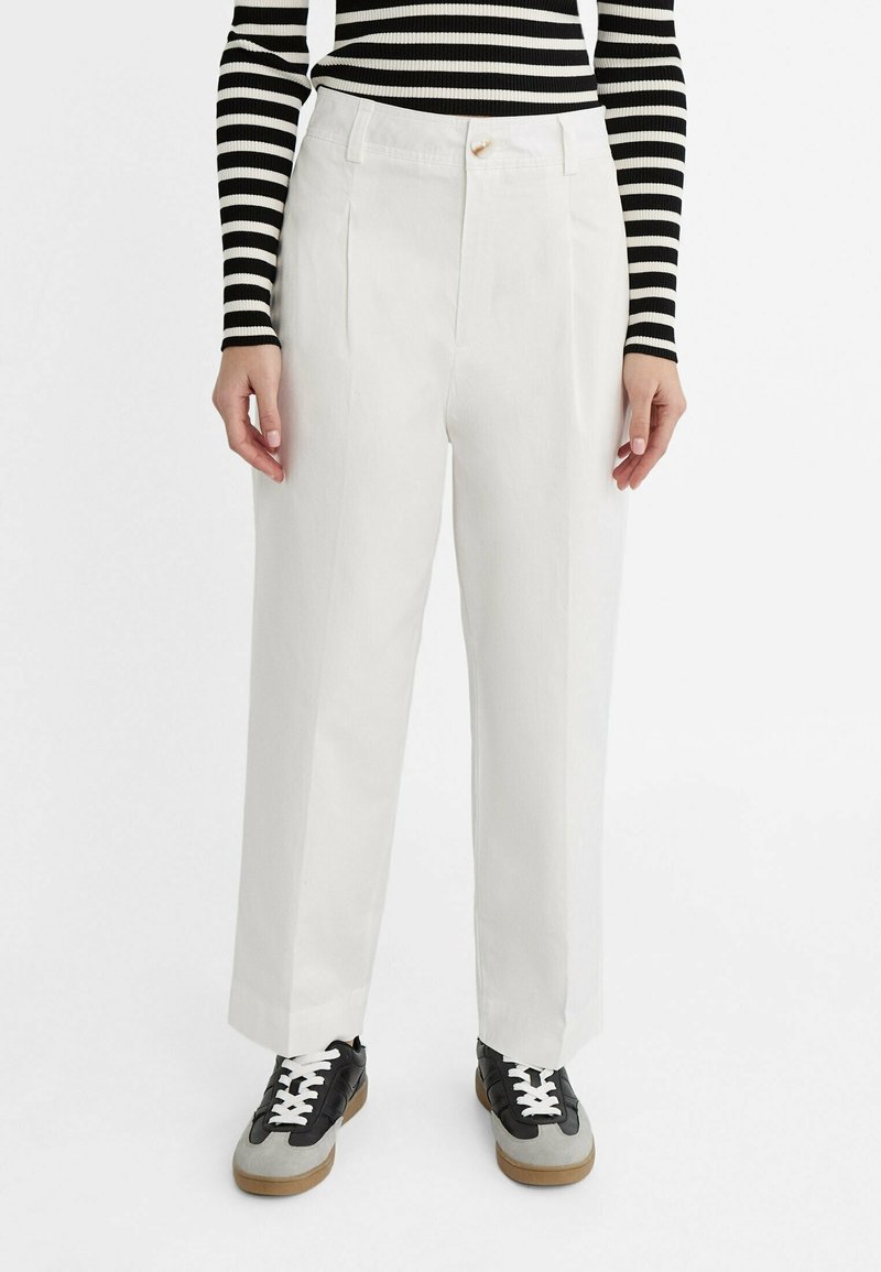 Pantalon blanc à jambes larges en tissu léger avec des plis marqués, porté avec un haut rayé noir et blanc et des baskets noires.