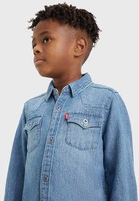 Koszula dżinsowa w jasnoniebieskim odcieniu, zapinana z przodu na guziki, z kołnierzykiem w kształcie ostrym, dwoma kieszeniami na piersi oraz metką z logo Levi's na lewej kieszeni.