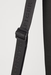 Schwarzer verstellbarer Riemen aus langlebigem Stoff, ausgestattet mit eingeprägtem Logo und einer schwarzen Kunststoffschnalle für sicheren Halt.