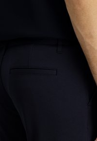Pantalones de vestir azul oscuro con una tela texturizada, que presentan un único bolsillo trasero con una solapa estrecha, corte entallado y acabado suave.