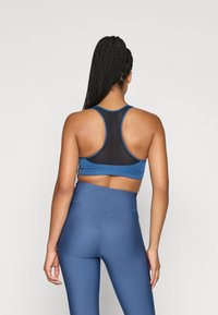 Μπλε αθλητικό αμάνικο μπλουζάκι με πλέγμα στην πλάτη και σχέδιο racerback, συνδυασμένο με μπλε κολάν με ψηλή μέση. Λείος υφασμάτιος χαρακτήρας και εφαρμοστό σχήμα.