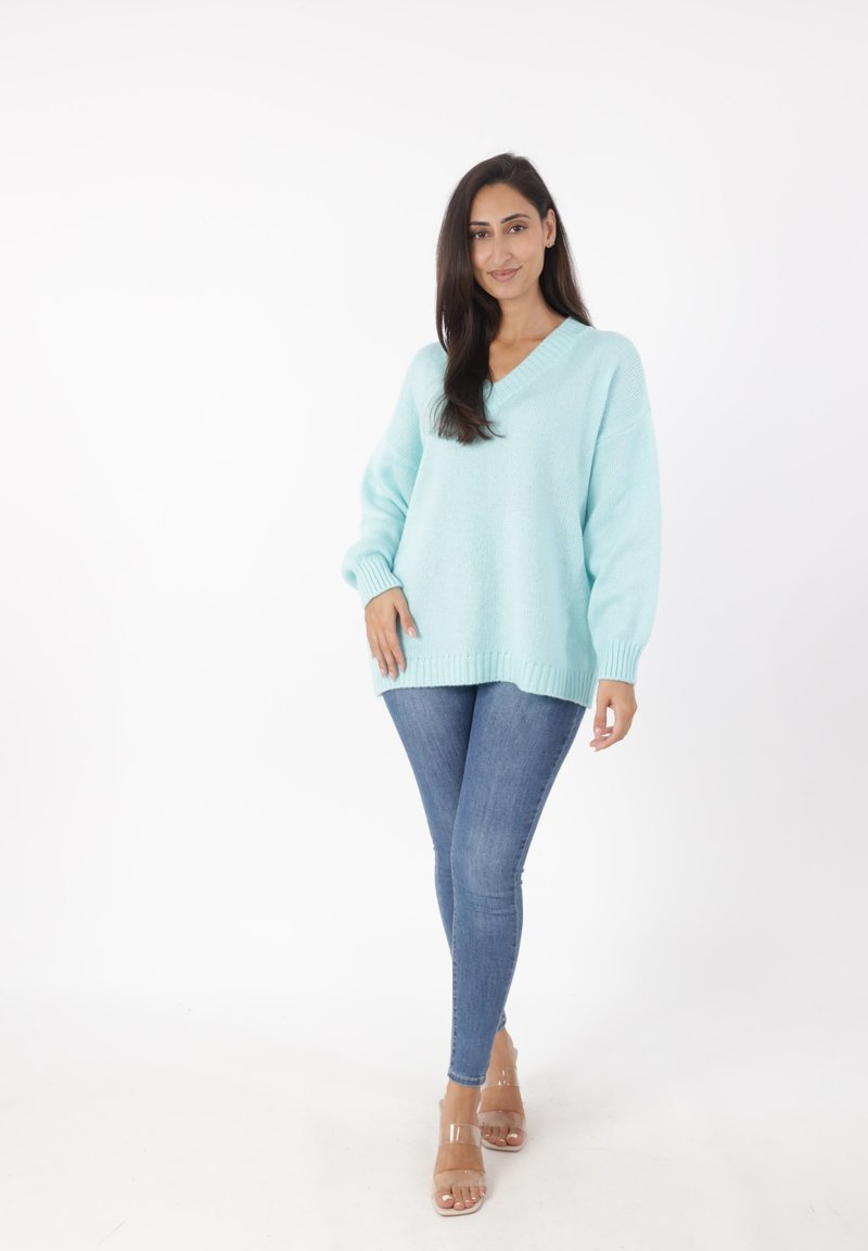 Maglione oversized verde menta con scollatura a V, polsini e orlo a costine. Abbinato a jeans blu aderenti e sandali con tacco trasparente.