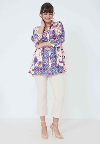 Multicolored patterned shirt with a collar and button front, paired with cream cropped pants and nude high heels. Smooth fabric texture.