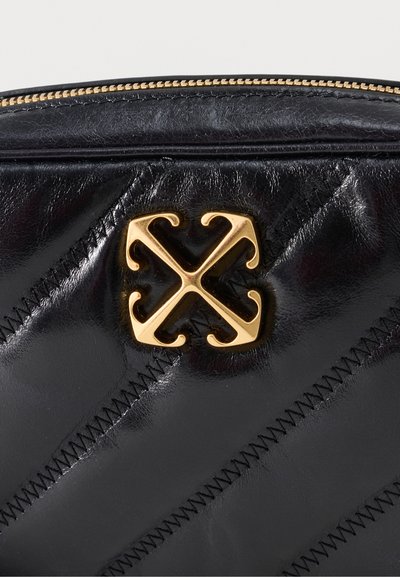 Μαύρη δερμάτινη τσάντα με καπιτονέ σχέδιο και διαγώνια ραφή, που διαθέτει χρυσό μεταλλικό έμβλημα λογότυπου και φερμουάρ με χρυσά δόντια στην πάνω άκρη.