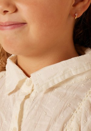 Goldener Creolen-Ohrring mit einem kleinen pinkfarbenen Edelstein. Texturiertes weißes Hemd mit geknöpftem Kragen und feinem Muster.