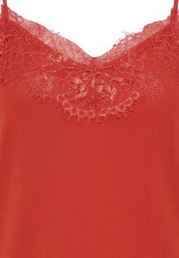 Haut rouge sans manches avec encolure en V détaillée par une bordure en dentelle florale le long de l'encolure et fines bretelles.