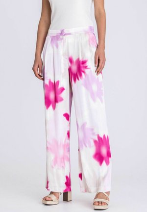 Frau trägt weiße, weit geschnittene Hosen mit großen rosa und lila Blumenmustern, kombiniert mit beigen Plateausandalen.