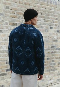 Pánska námornícka košeľa s vzorom vyrobená z jemnej látky, s geometrickými vzormi v rôznych odtieňoch modrej, s golierom a gombíkmi na manžetách.