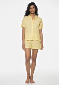Gula rutiga pyjamasar med en knäppbar t-shirt med kort ärm och matchande shorts, tillverkade av lätt tyg med en strukturerad yta.