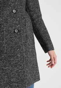Cappotto grigio in misto lana con superficie testurizzata, due bottoni neri e tasche laterali, dal taglio rilassato e con maniche a polsino.