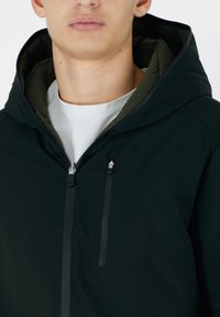 Giacca nera con cappuccio, dotata di chiusura con zip, con un rivestimento interno verde a contrasto e due tasche con zip sul davanti per praticità.