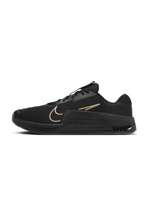 Zapatilla deportiva negra con parte superior de malla, logotipo beige en forma de swoosh, media suela gruesa y texturizada, y cordones negros, mostrada de perfil sobre fondo blanco.