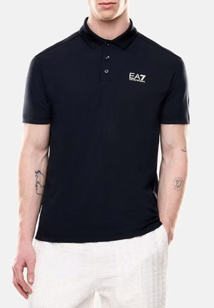 Polo de color azul marino con una tapeta de dos botones y el logo de EA7 en la parte superior izquierda. Hecho de una tela suave y de manga corta, combinado con pantalones blancos texturizados.