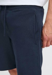 Shorts en coton bleu marine avec une taille élastique, des poches latérales et une texture lisse. Dotés d'un cordon de serrage et d'une coupe décontractée.