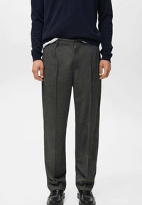 Pantalones de lana gris carbón con un diseño de pierna recta, que presentan pliegues, bolsillos laterales y una cinturilla tradicional. Llevados con un suéter azul marino.