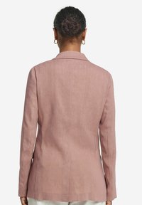 Ljusrosa blazer gjord av texturerat tyg, med slagkrage, långa ärmar och en figurnära silhuett med bakslits.