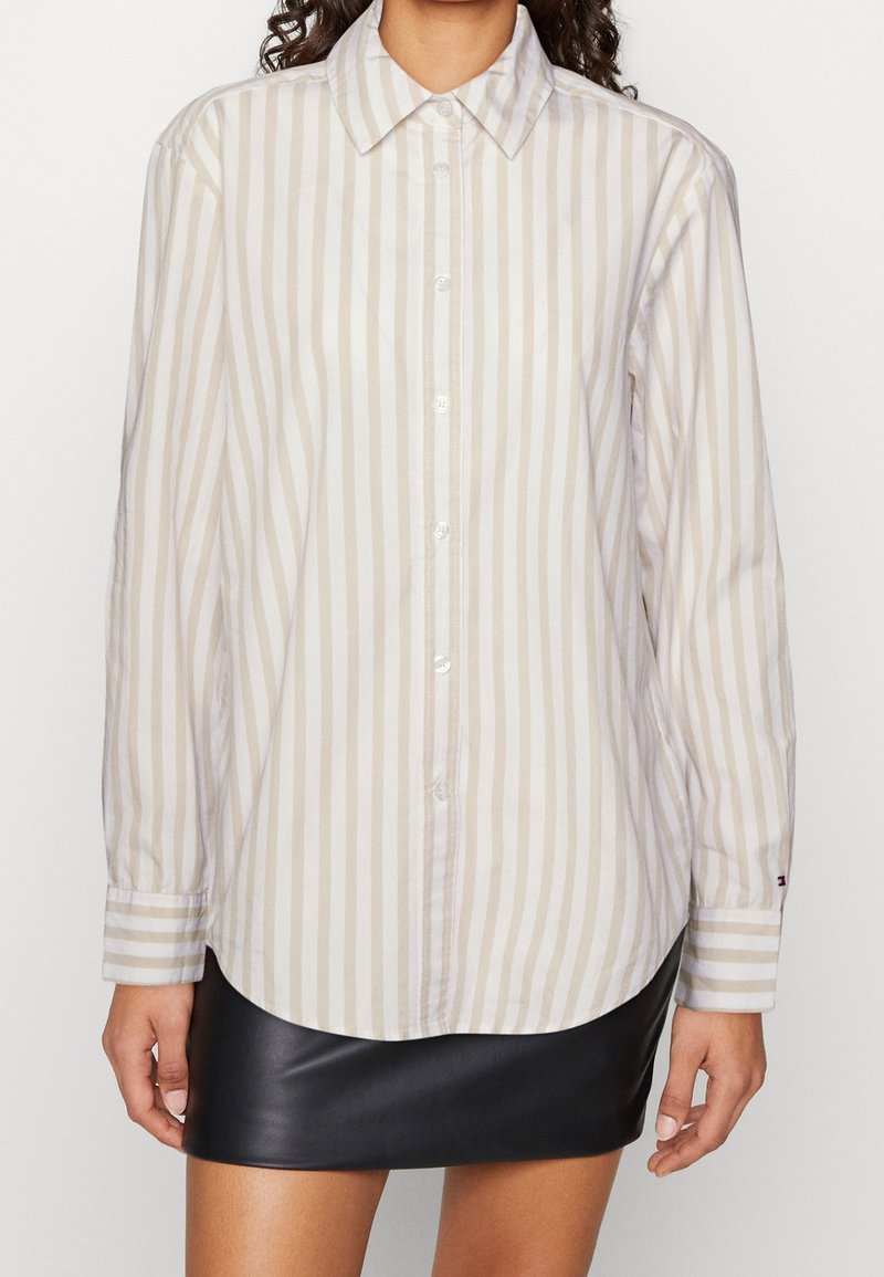 Mujer vistiendo una camisa de botones de rayas verticales beige y blancas con cuello puntiagudo y falda de cuero negra.