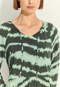Dlouhé šaty se zeleným a černým tie-dye vzorem, s výstřihem do V a stahovací šňůrkou s růžovými akcenty. Měkká tkanina, volný střih.