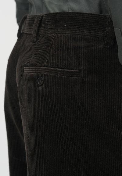A fekete kordbársony nadrág texturált, bordázott felülettel, gombos hátsó zsebbel és egyenes fazonnal rendelkezik, amelyet tiszta vonalak emelnek ki.