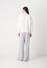 Felpa bianca con fondo e polsini a costine abbinata a pantaloni della tuta grigi larghi. Il tessuto appare morbido e liscio. Design semplice e minimalista.