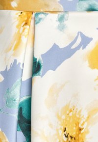 Tessuto con motivo floreale che mostra tonalità di giallo, verde e blu con una superficie texturizzata; presenta morbidi drappeggi e dettagli a pieghe.
