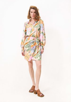 Robe florale dans des couleurs pastel, avec un col, des manches longues et un détail de ceinture; associée à des sabots à talons ouverts marron.