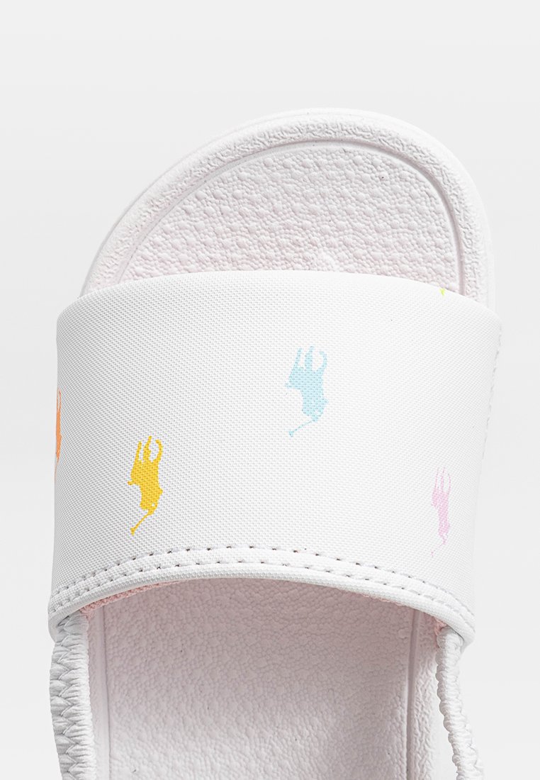 Sandale blanche avec une semelle intérieure douce et texturée et une large lanière ornée de motifs colorés de petits lapins sautant en rose, bleu, orange et jaune.