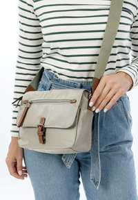 Borsa a tracolla beige realizzata in tessuto con chiusura a patta, tasca con zip e accenti in pelle marrone; presenta una tracolla regolabile.